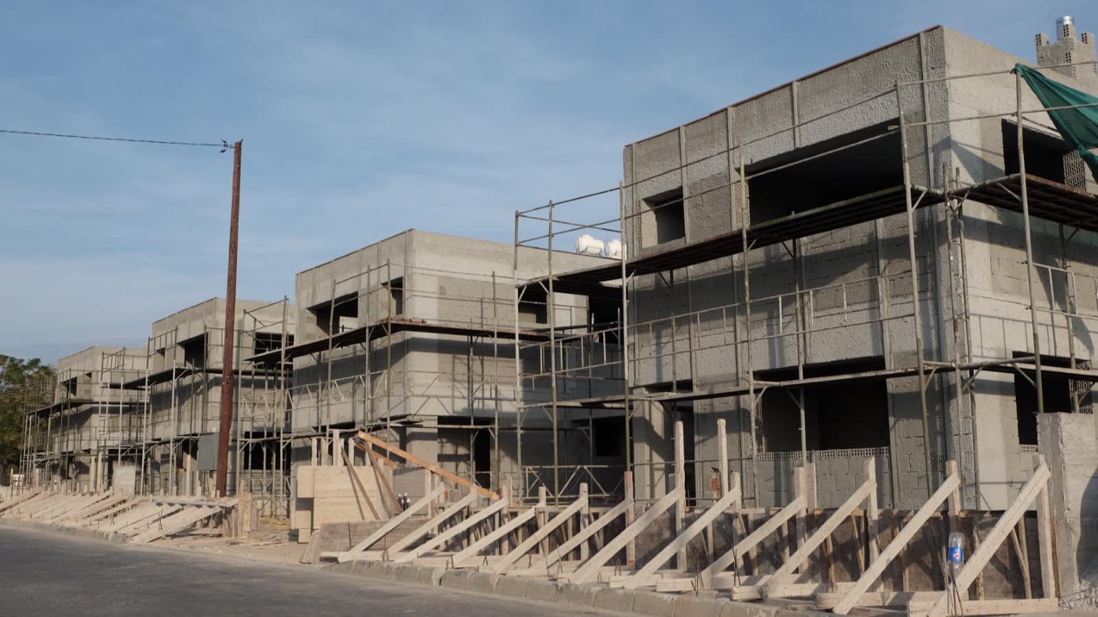 A terrace of new Cypriot houses under construction, still in blockwork with scaffolding and timber props along the street