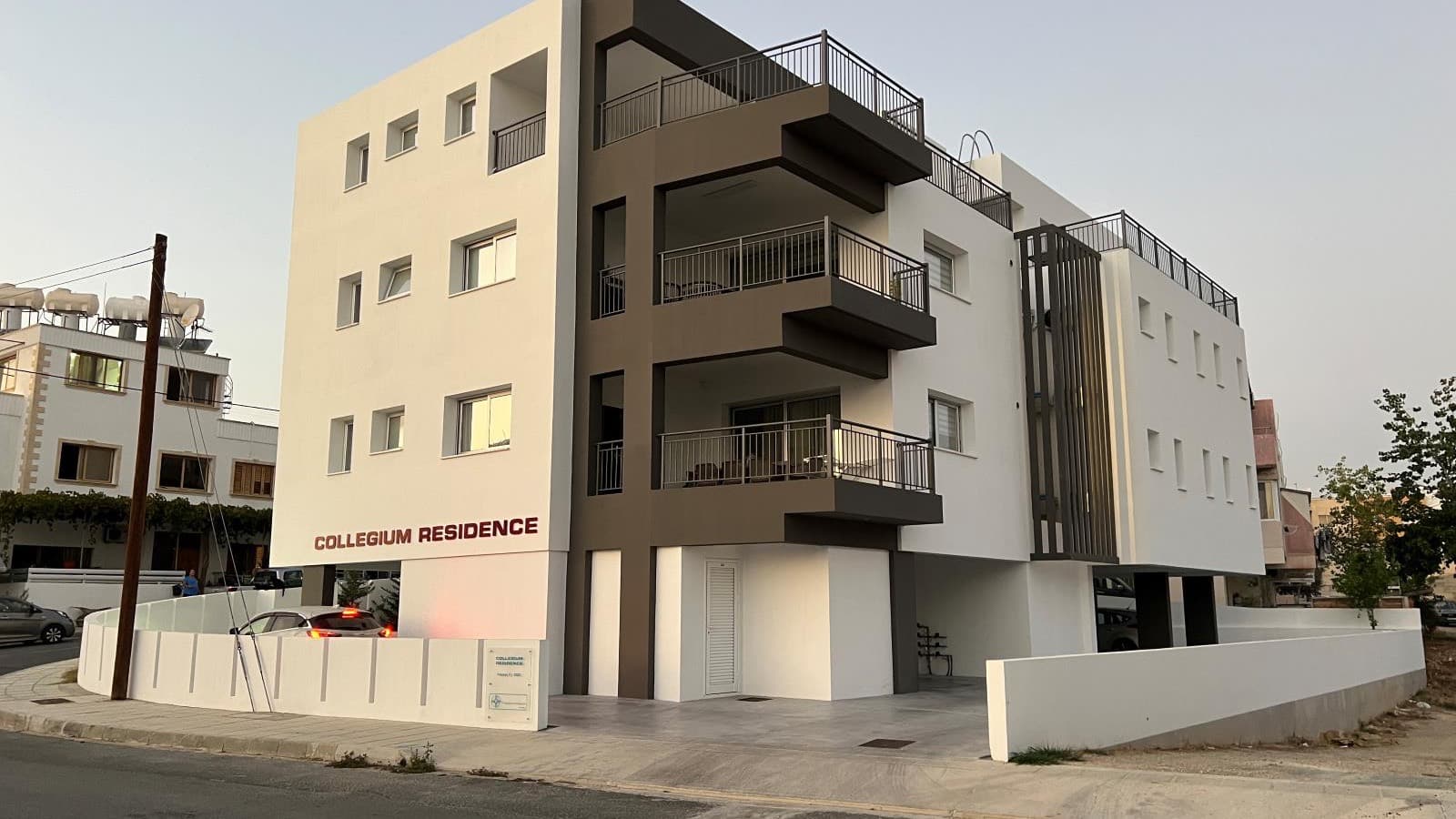 A completed and occupied apartment building in Paphos at dusk, with cars parked outside and lights on in the windows